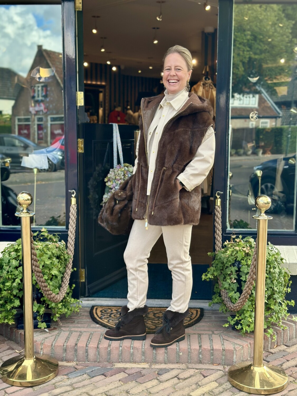Lichte vrouw in winterjas voor modieus boetiekje met gouden plekschermen en groene planten.